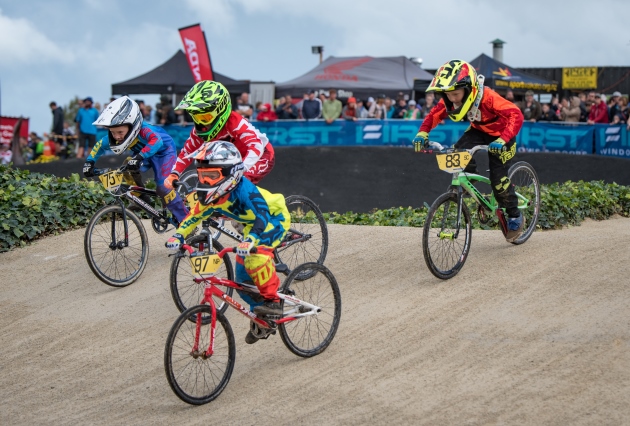 Four young BMX riders, with full BMX riding gear on their BMX bikes riding down a slope